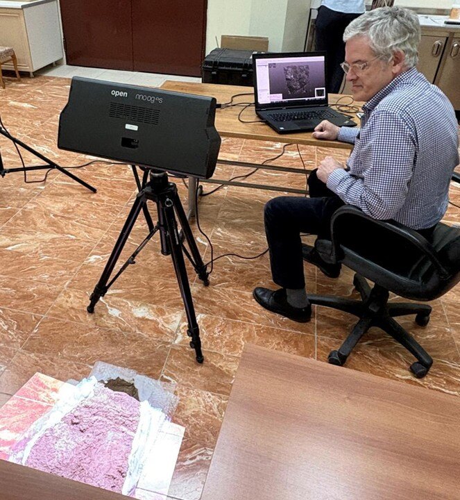 A person sits beside a computer and a scanner on a tripod, overseeing the scanning of artifacts.