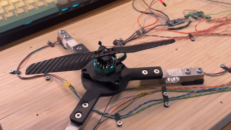 A 3D-printed propeller is shown mounted on a motor on a triangular test stand. Each corner has a load cell, and wires run from it to the right.