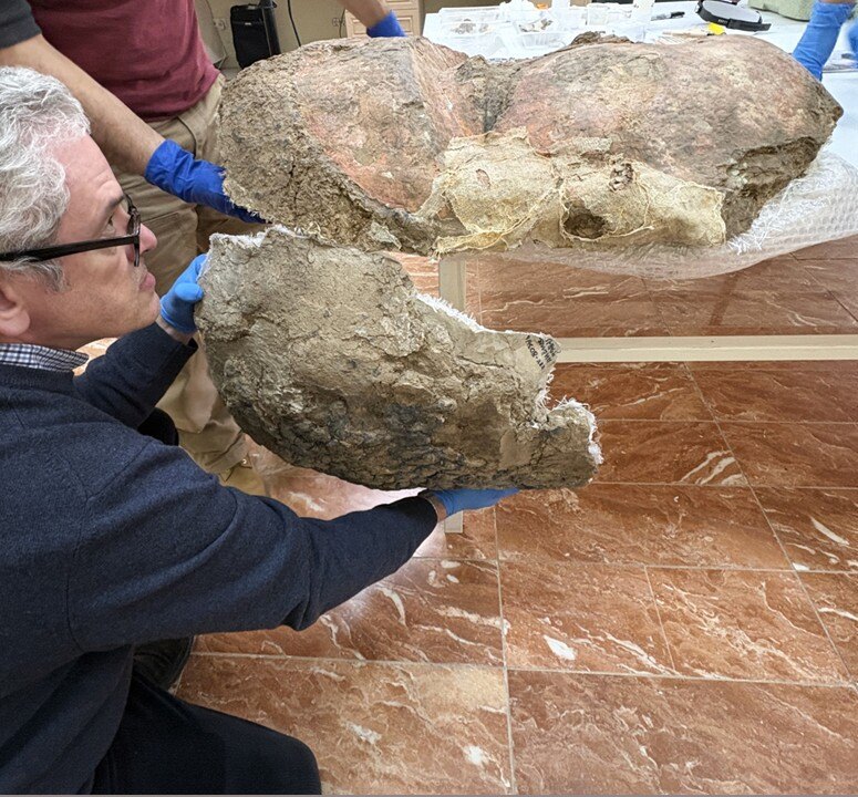 A person kneels and holds a portion of the artifact up near the larger, connective piece.