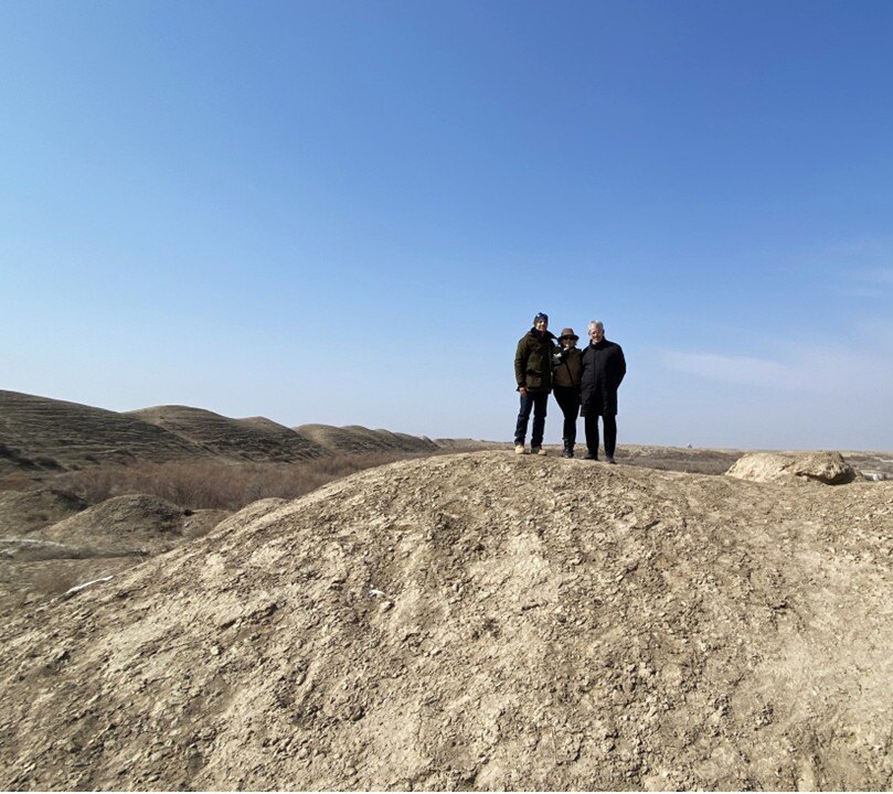 Three people stand close for a photo on top of a barren hill.