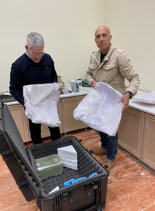 Two people hold packing material removed from large, padded storage containers.